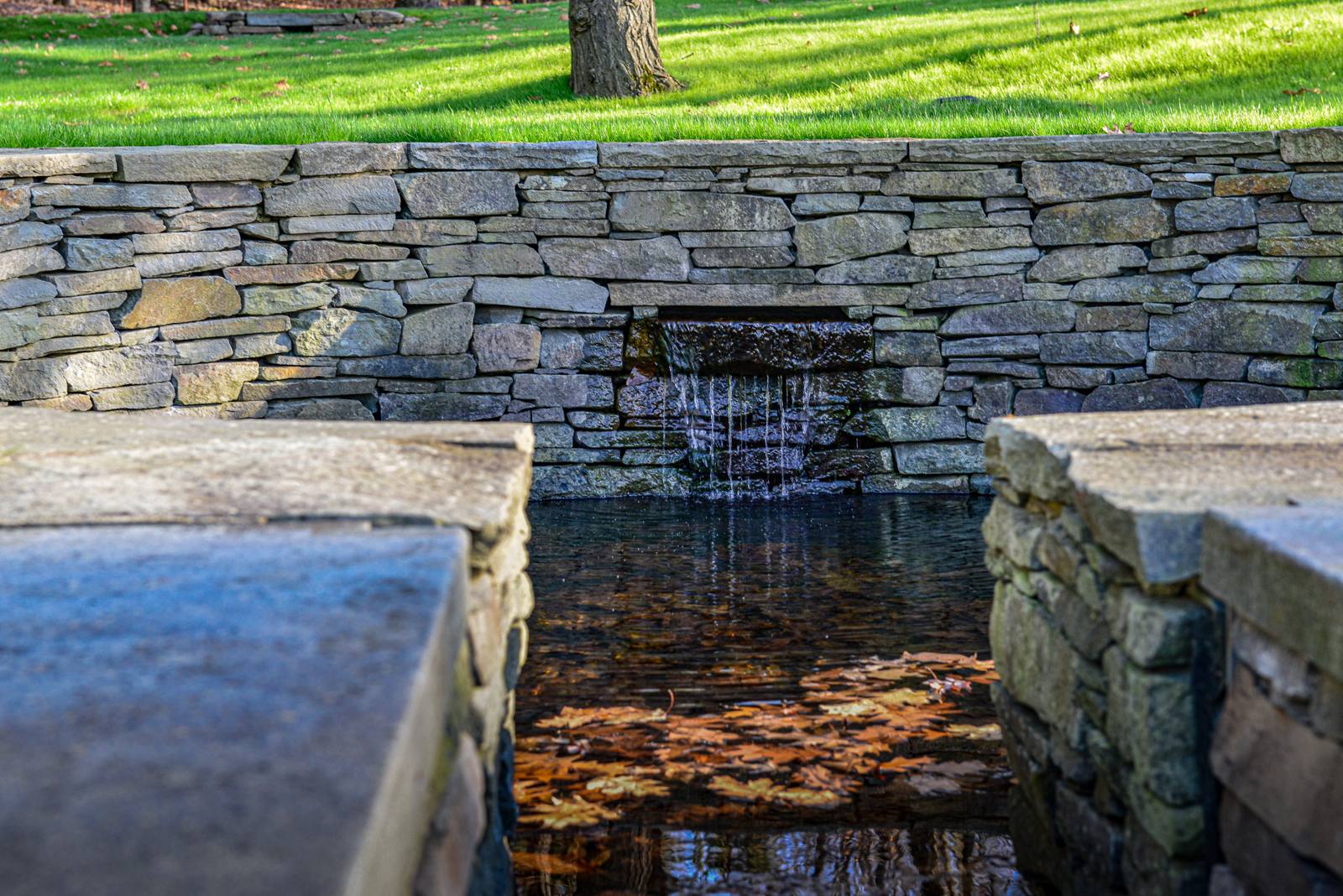 Waterfall spilling from a dry-laid stone wall into a narrow channel