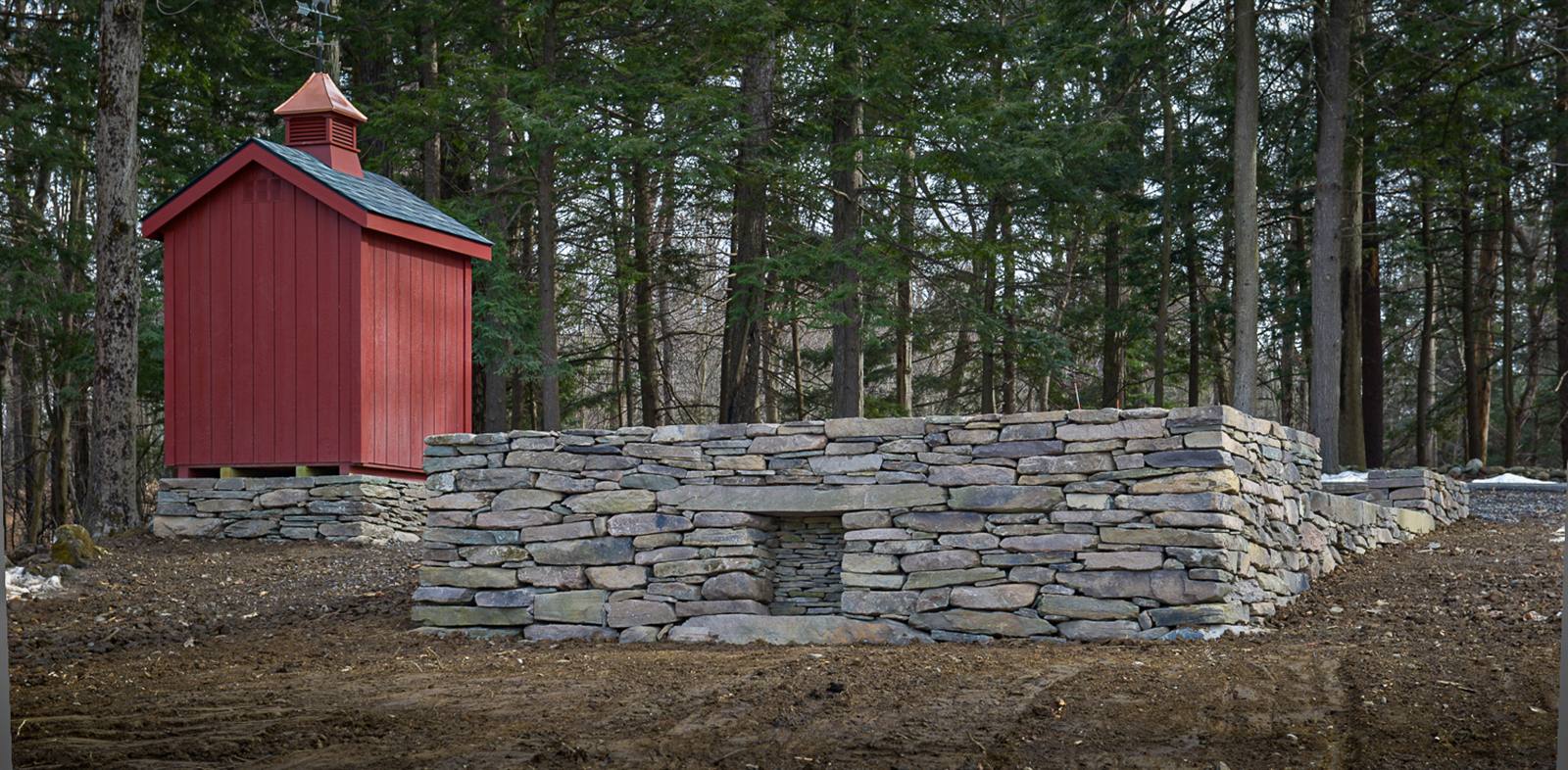 Red cupola outbuilding beside a dry-laid stone wall with an arched niche