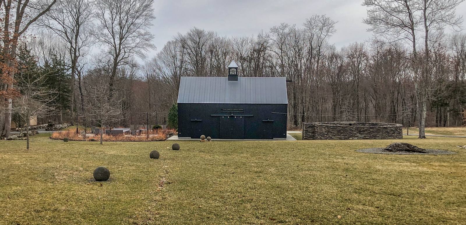 Black barn across the lawn with stone spheres and a circular stone ruin
