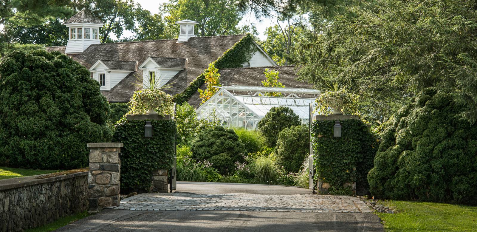 Ivy-covered gate piers and a greenhouse beyond a cobblestone drive entrance