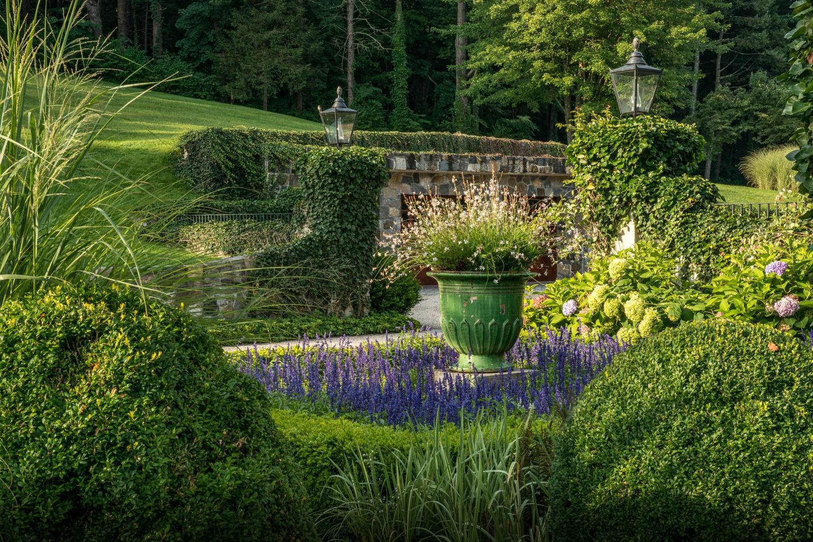 Green urn with gaura and hydrangea before a stone garage with ivy-covered piers