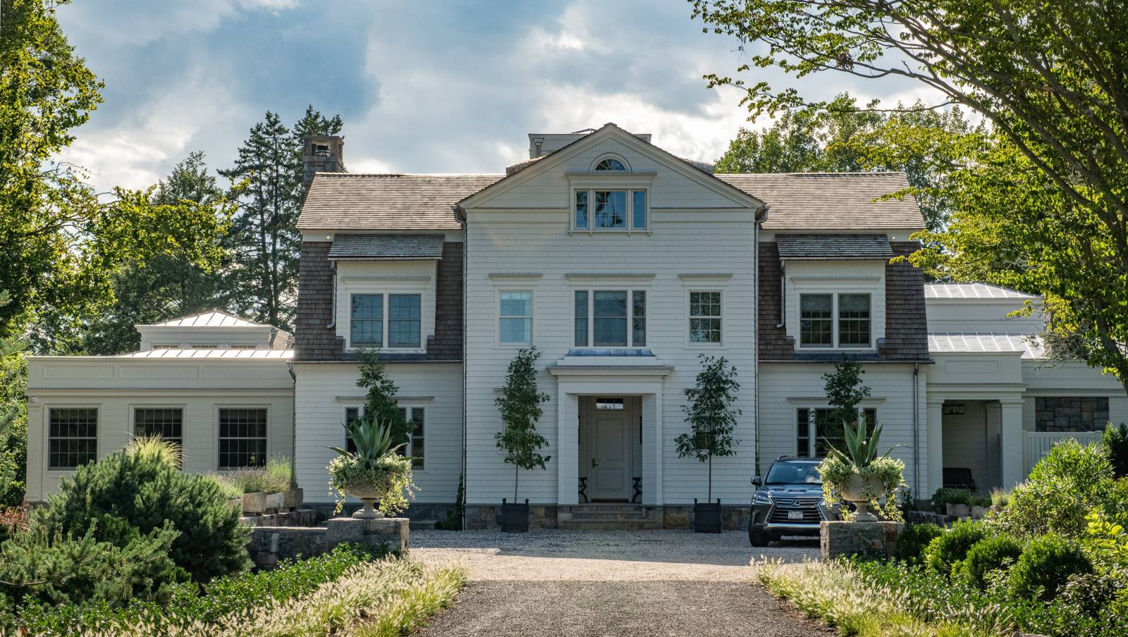 Entrance front of a shingled house with a gravel court and urns