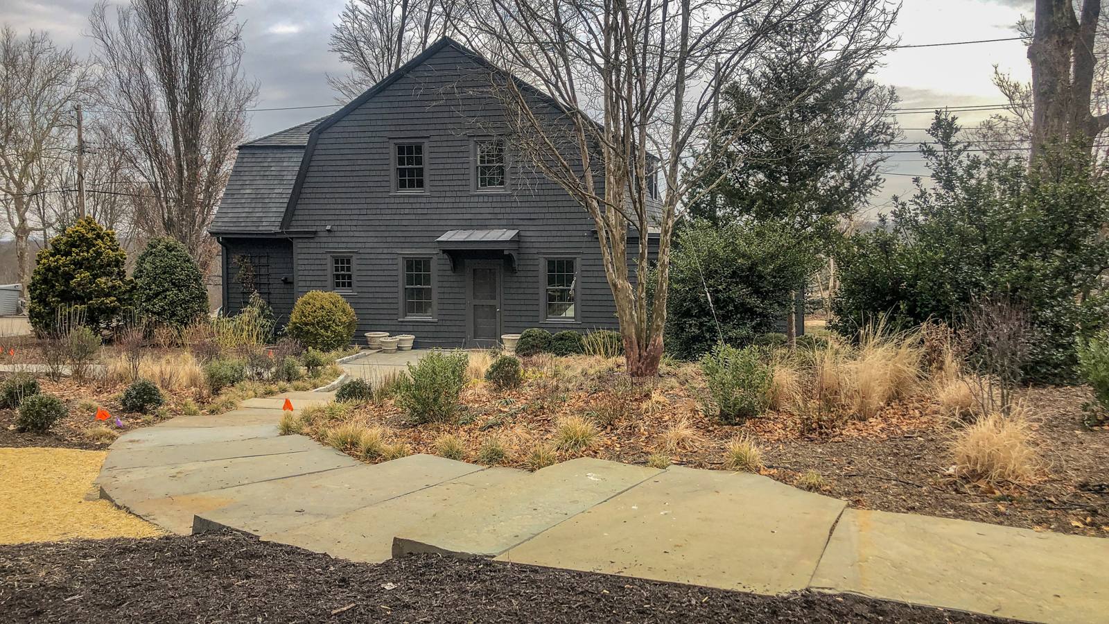 Stone walk and plantings in winter in front of a dark shingled house