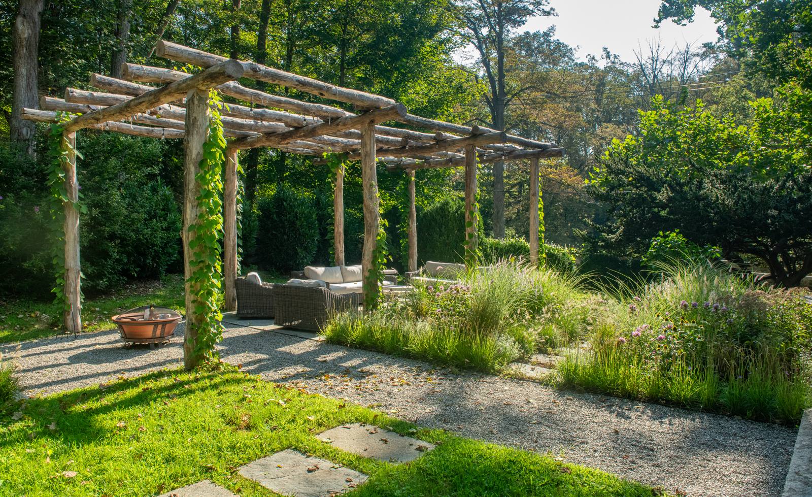 Rustic locust-log pergola with seating, a fire bowl and a naturalistic border of grasses and perennials