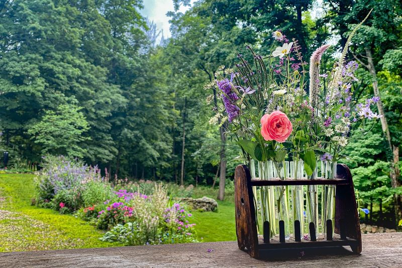 Garden flowers in glass tubes on an antique wooden rack overlooking a perennial border and woodland