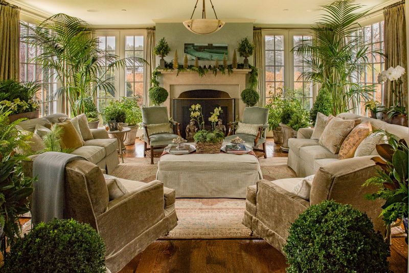 Sunlit living room with kentia palms, boxwood spheres, ferns and orchids framing the fireplace