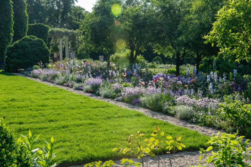 Backlit flower border and lawn leading toward a vine-covered pergola
