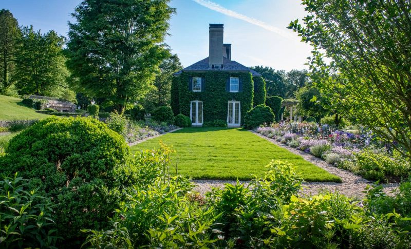 Ivy-covered house at the end of a lawn flanked by perennial borders