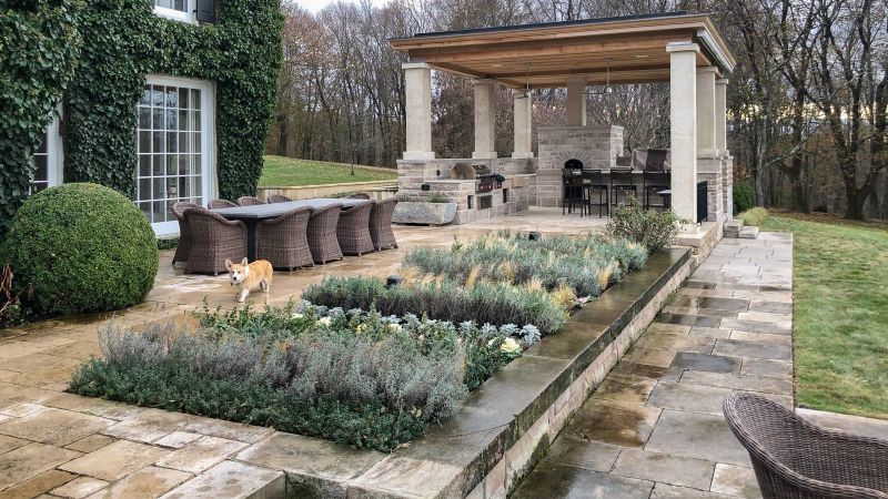 Pavilion and outdoor kitchen across a terrace of lavender and grasses, with a dining table beside the ivy-covered house