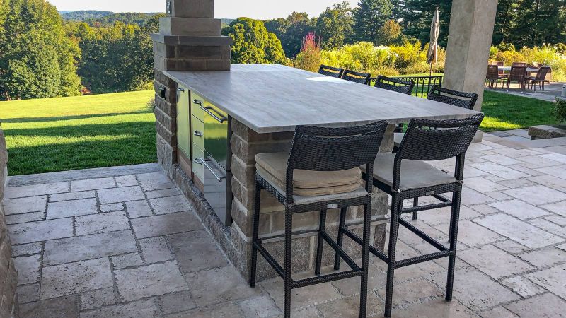 Stone bar with stainless drawers and wicker stools looking out over the lawn and hills