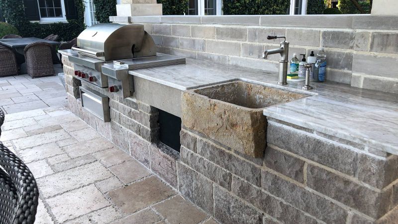 Gas grill and carved stone sink set into a limestone counter with a quartzite top