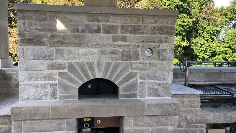 Wood and gas-fired pizza oven in limestone with a radiating arch, beside the Brazilian parrilla