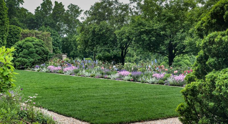 Perennial border of pink, blue and coral flowers along a gravel path and lawn