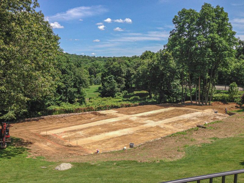 Beds and gravel paths staked out and graded, seen from above with an excavator at the edge
