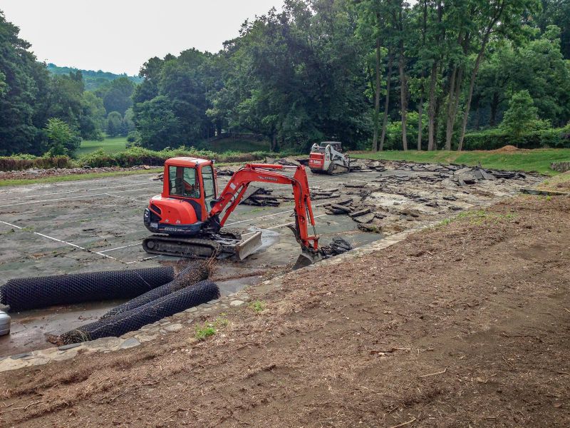 Mini excavator and skid steer removing the broken asphalt of the old tennis court