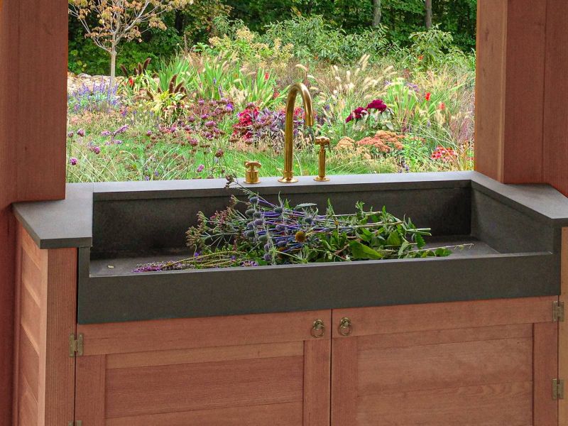 Wide dark stone flower-arranging sink with brass fittings in the gazebo, overlooking the garden