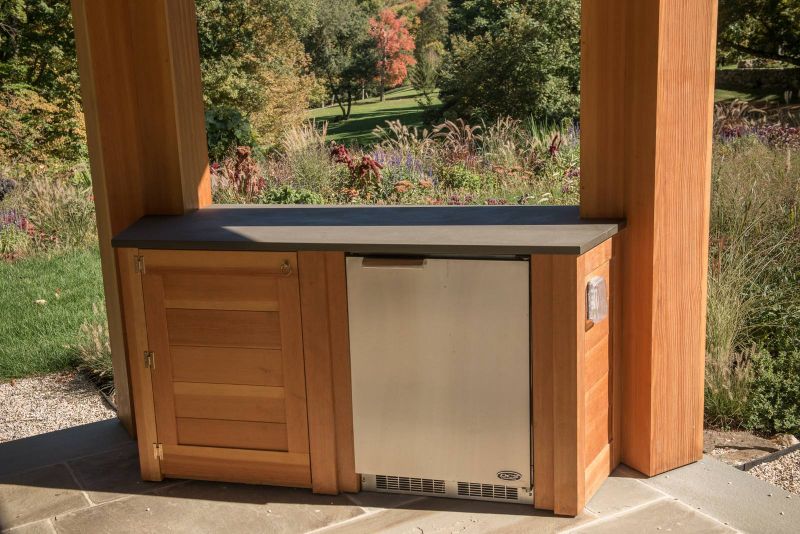 Cedar cabinet and built-in refrigerator beneath a stone counter in the gazebo