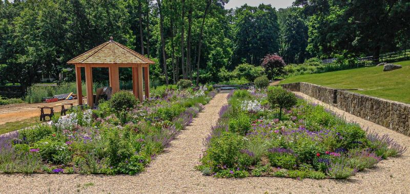 New gazebo and freshly planted beds divided by a gravel path beside the stone retaining wall