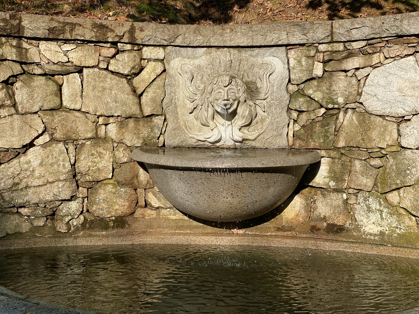 Carved stone mask fountain spilling into a granite basin and pool