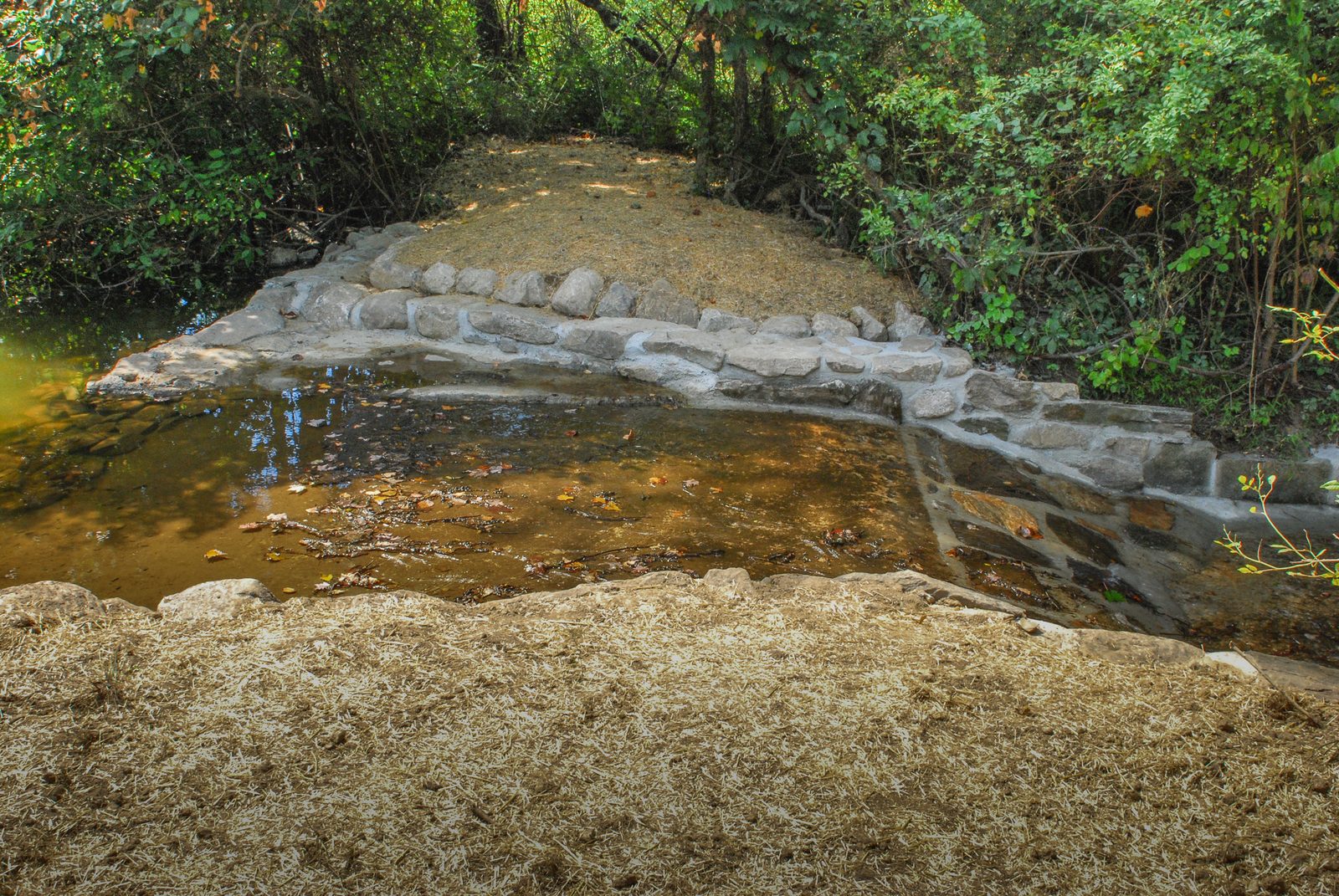 Stone-walled spring pool with straw-mulched banks after construction