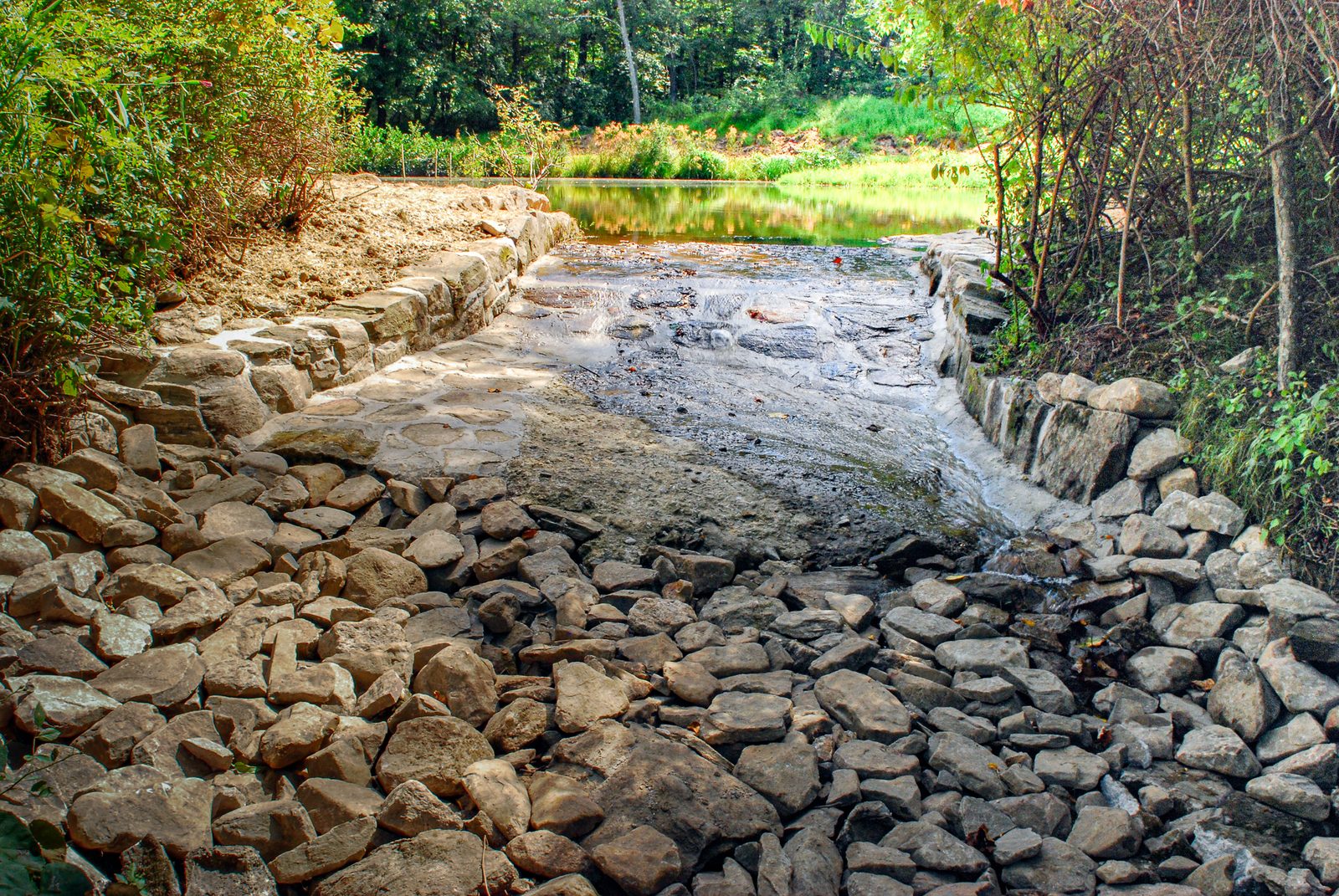 Stone-lined spring channel flowing toward the pond over a rock apron