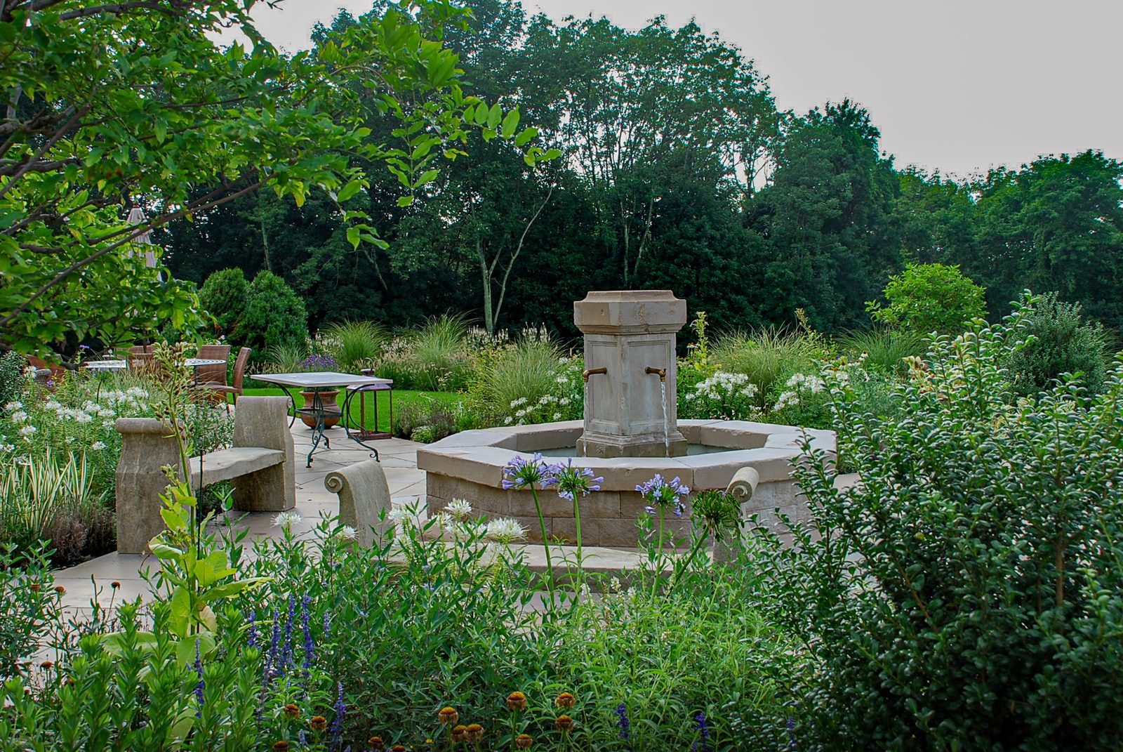 Octagonal limestone fountain on a terrace among white and blue flowers