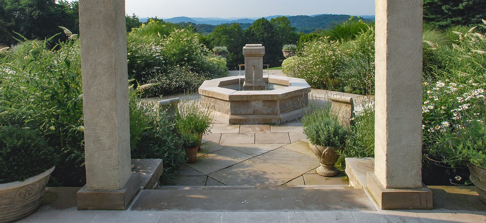 Limestone terrace fountain framed by stone columns with distant hills beyond